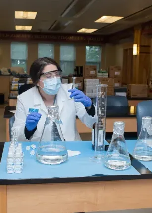 A pharmacy student examines beakers while making hand sanitizer