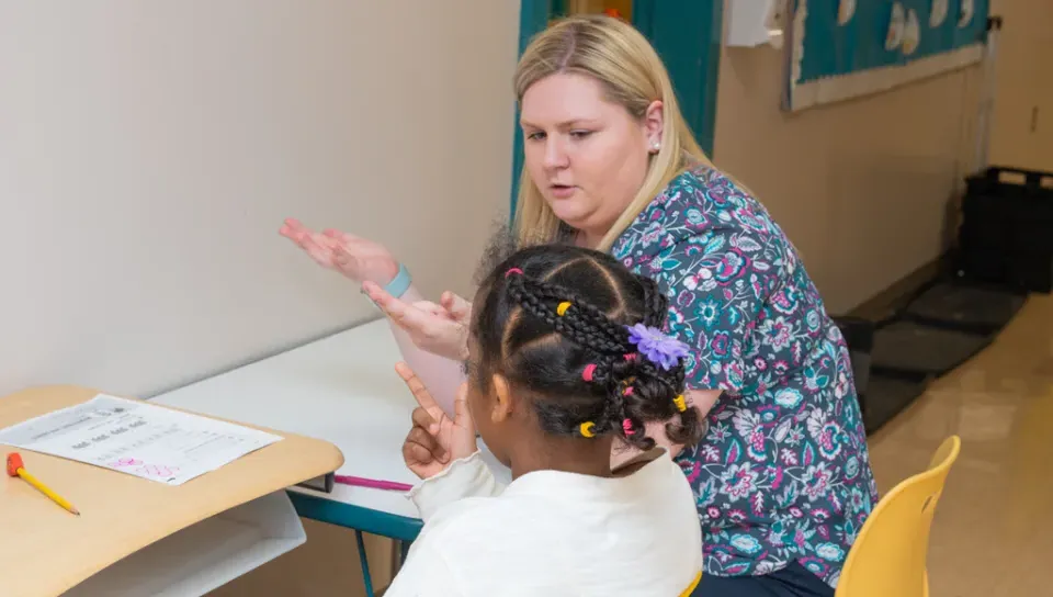 An education student helps an elementary school student count with their hands